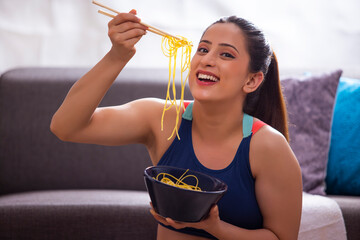 Young woman eating noodles with chopsticks