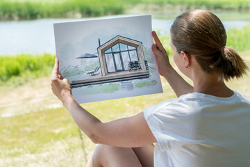 Architect holding barn house  hand drawn sketch in front of a plot of land.