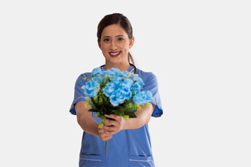 Portrait of smiling female nurse with flower bouquet against white background