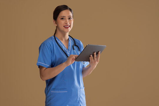 Portrait Of Female Nurse In Blue Scrubs Standing With A Digital Tablet In Her Hand