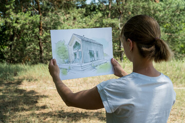 Architect holding barn house  hand drawn sketch in front of a plot of land. © Volodymyr Herasymov