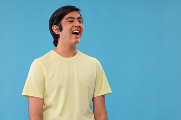 Portrait of cheerful teenage boy looking away against blue background