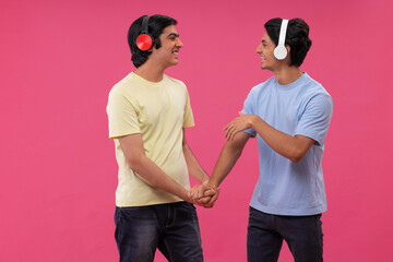 Two happy friends listening to music against pink background