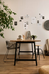 The stylish composition of cozy office interior with metal chair, wooden table, plants, pictures and personal accessories. Home decor. Template.