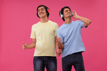 Two happy friends listening to music against pink background