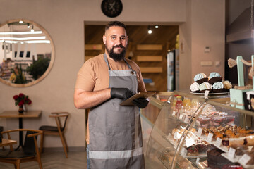 Portrait of successful young Indian cafe owner standing using digital tablet. small business owner...