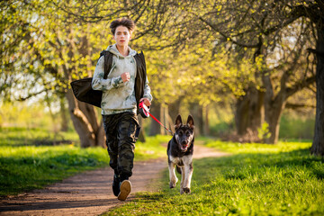 a boy with a dog walk in the park on a sunny spring evening, run along the road. Friendship of man and animal, healthy lifestyle.