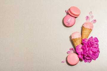 Ice cream waffle cones with macarons on a stone background. Sweet dessert, peonies flower petals
