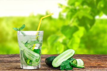 Refreshing drink with cucumber and mint, in a glass with a straw, next to ice cubes, against a green background