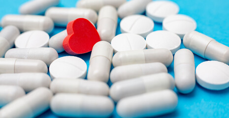 Red pill in the shape of a heart on a background of white pills and a blue background. The concept...