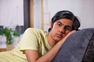 Close-up portrait of teenage boy leaning on sofa at home 