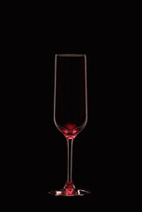 Empty champagne flute backlit with red light and isolated on black background. Beverage glassware concept. Copy space.