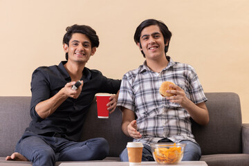 Two happy teenage boys eating fast foods and watching TV together at home
