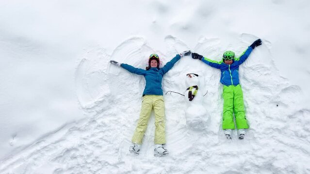 Woman and a boy lay in the snow waving hands view from above
