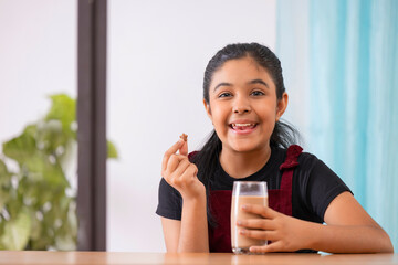 Portrait of cheerful little girl having breakfast with cereal and chocolate milkshake at home 