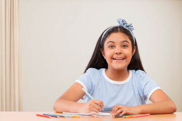 Portrait of cheerful girl writing on notebook against white background