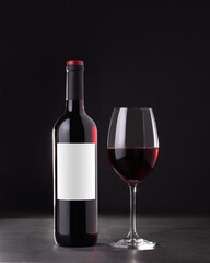 Single red wine bottle with blank label for mockup and glass of red wine on dark gray background