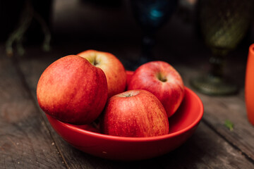 Four red apples lie in an orange plate on a wooden table