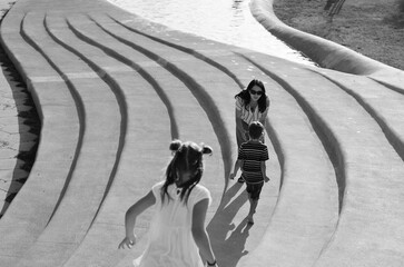 Happy family lifestyle and holiday concept. Mother, little boy, girl sitting, walking in old city, street. Ride scooters. laughing on a summer sunny day. Having fun