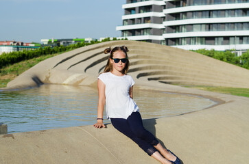 Fototapeta premium Happy family lifestyle and holiday concept. little girl walking, playing in fountain in city, street. laughing on a summer sunny day. Having fun. Staying cool