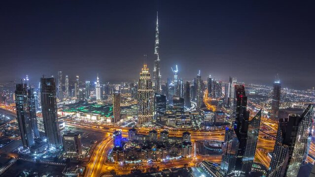 Aerial view of tallest towers in Dubai Downtown skyline and highway night timelapse panorama. Financial district and business area in smart urban city. Skyscraper and high-rise buildings