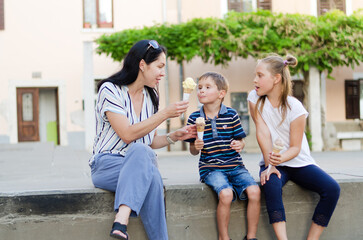 Happy family lifestyle and holiday concept. Mother, little boy, girl sitting, eating ice cream in old city, street. laughing on a summer sunny day. Having fun. Staying cool