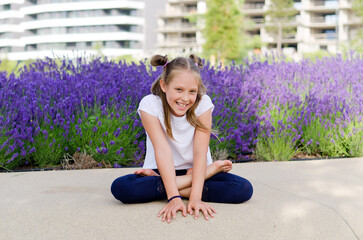Happy lifestyle and holiday concept. little girl playing in city, park, doing yoga poses. Field of lavender flowers. summer sunny day. Having fun