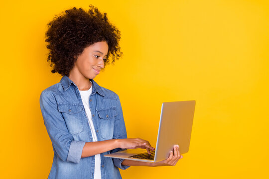 Portrait of attractive cheery skilled teen girl using laptop writing e-mail isolated over shine yellow color background