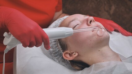 A beautician makes a darsonvalization of the face of a young girl with problem skin.