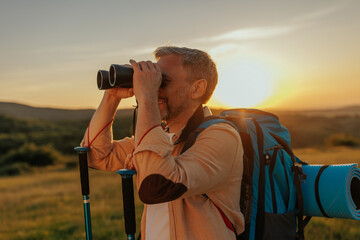 Middle aged man hiking is looking for direction with binoculars