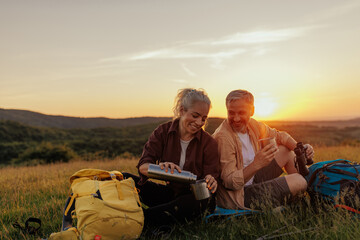 Traveler couple sitting on meadow and drinking hot beverage