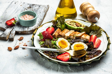 Keto breakfast two eggs, avocado, strawberry, grilled chicken fillet, nuts and fresh salad, Ketogenic diet. Plate with keto diet food. Healthy food concept, top view