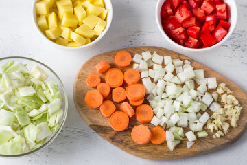Chopped ingredients for a vegetable dish: potatoes, cabbage, carrots, onions, garlic, tomatoes on a light blue background. Cooking delicious vegan food