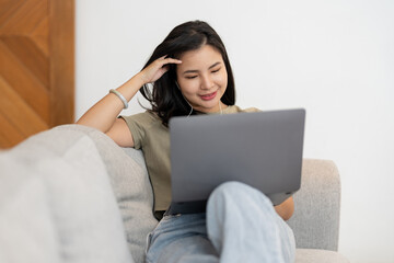 young asian woman laying in living room on sofa studying with headphones and computer, stay at home concept