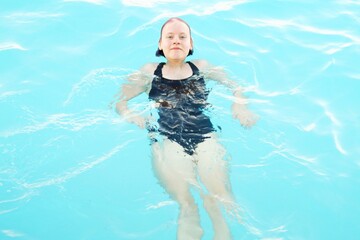 Girl in a black swimsuit relaxes in the pool.