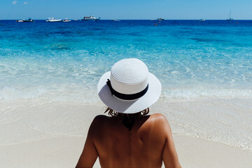 Fototapeta na wymiar Young woman in white hat sitting at the seashore is enjoying vocation somewhere in Dominican republic
