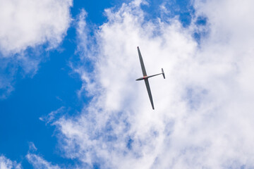 Sailplane flying under white clouds in blue sky