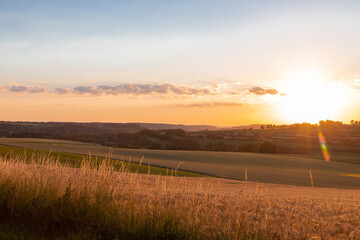Obraz premium Sunset over the rolling hills in Elkenrade in the of south Limburg in the Netherlands with a spectacular view over the fields, full of wheat and some amazing beams from the sun during golden hour.
