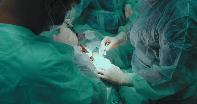 Team of surgeons in sterile suits perform blepharoplasty surgery. The surgeon makes an incision in the crease of the eyelid with a surgical instrument