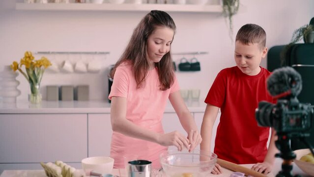 Boy and girl recording culinary blog at home. Girl breaks raw egg into bowl. Steadicam shot.