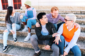 Group of friends enjoying the weekend sitting outdoors. Multiethnic people talking in stairs.