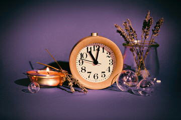 Still life arrangement with wood alarm clock on purple background. Dry lavender, tea light with...