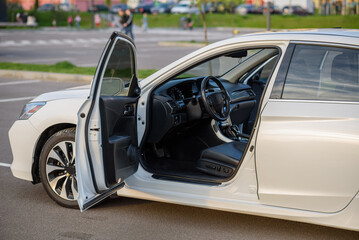 Side view of the open driver's door, mirror, dashboard of the car. Left front door. A new modern shiny parked white car. Interior luxury car with tinted glass standing at parking. Modern car exterior.