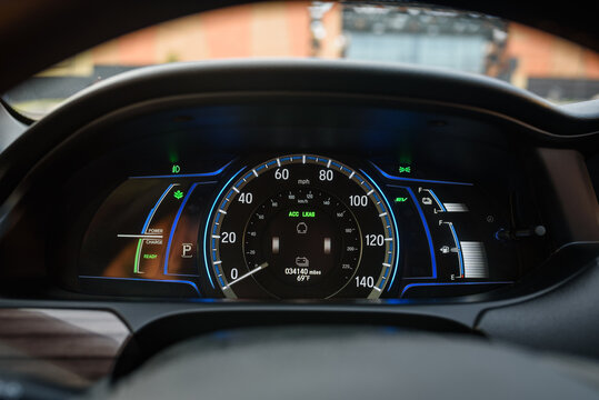 Car counter showing power monitor of engine and battery use in a hybrid vehicle. Panel with illuminated display indicating battery charge, energy level, speedometer, tachometer, odometer, fuel gauge.