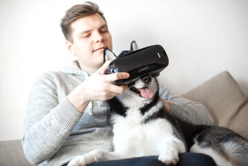 Young man and siberian husky dog using vr goggles sitting on sofa at home