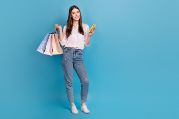 Full length body size view of attractive cheerful trendy girl holding bags buying app 5g isolated over bright blue color background