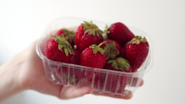 Hand holding transparent plastic box with fresh strawberries on a white background. 