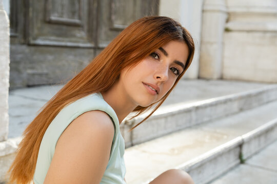 portrait of pretty redhead woman looking at camera on blurred venetian street.