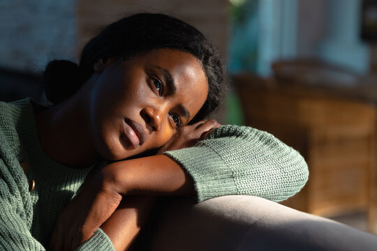 Lonely african american young woman looking away while resting head on sofa at home, copy space