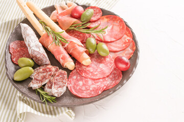 Charcuterie plate with different types of sausages - salami, bresaola, proscuitto served with grissini bread sticks. Menu background. Traditional italian antipasti at white table